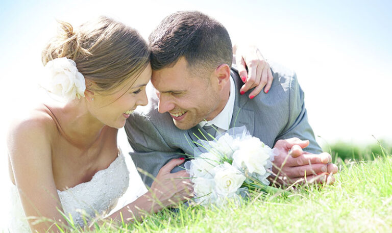 Im Gras liegendes Strahlend lächelndes Brautpaar im Gegenlicht