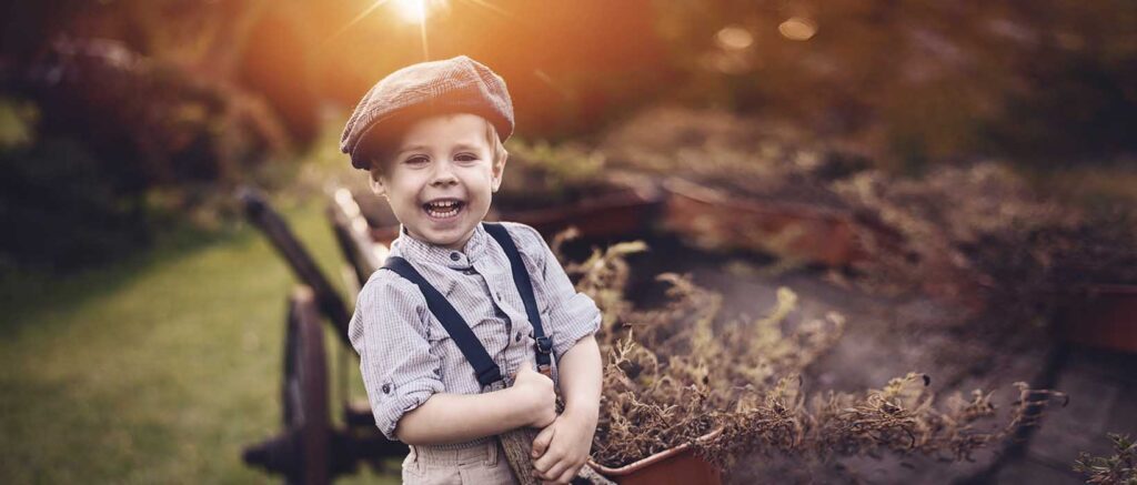 inszenierte Luxus-Fotografie: kleiner Junge im Retro-Style forografiert im Freilandmuseum sich an ein hölzernes Pferdefuhrwerk klammernd